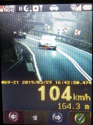 Zdjęcie zrzut z urządzenia do pomiaru prędkości pojazdów. Zdjęcie przedstawia pojazd marki mercedes na drodze. Na dole wskazana jest prędkość z jaką się porusza 104 km/h