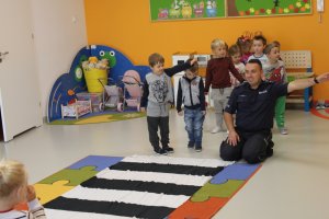 policjant w przedszkolu uczy dzieci jak przechodzić po pasach