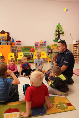 policjant rozmawia z dziećmi. Siedzą na dywanie